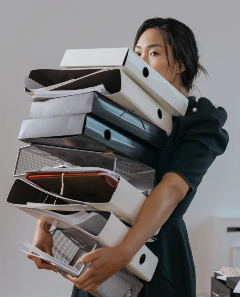 Busy Asian woman carrying giant pile of binders for work